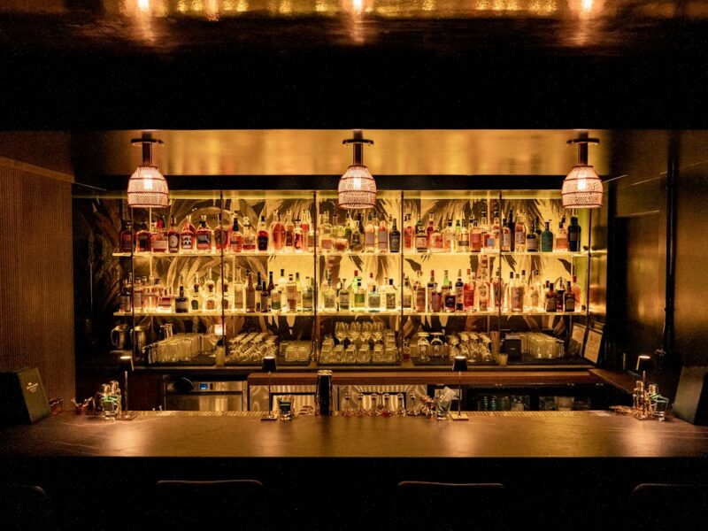 a dimly lit bar with a long counter and shelves of bottles behind it