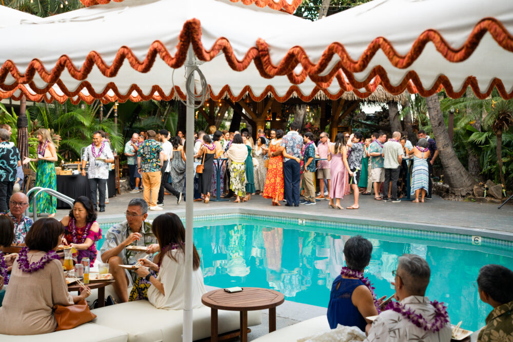 A group of people gathered around a pool with tables and umbrellas