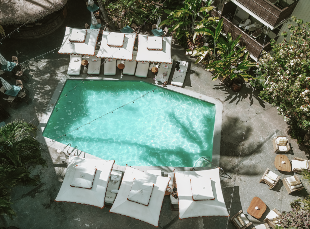 An aerial view of a pool with white lounge chairs and umbrellas surrounded by plants.
